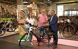 Peter Heinemann (mitte) nimmt sein E-Bike aus den Händen von Kathrin Weickmann und Andreas Marx von LOTTO Hessen entgegen